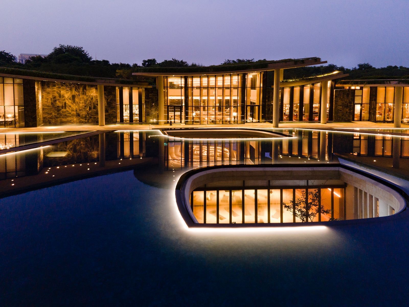 Clubhouse pavilion lit at dusk over a reflecting pool